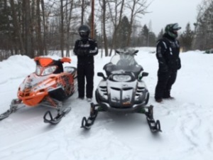two men standing next to snowmobiles